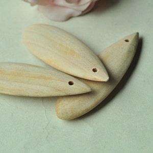 May include: Three wooden teardrop-shaped pendants with a hole at the top. The pendants are light brown and have a smooth, polished finish.