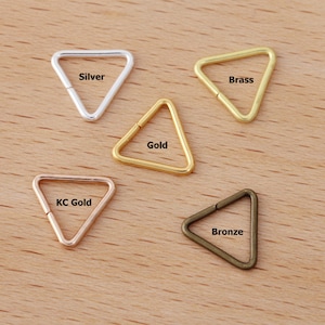 Peut inclure: Collection de cinq anneaux triangulaires en métal argenté, doré, laiton, or KC et bronze. Chaque anneau est ouvert d'un côté. Le texte indique la couleur de chaque anneau.