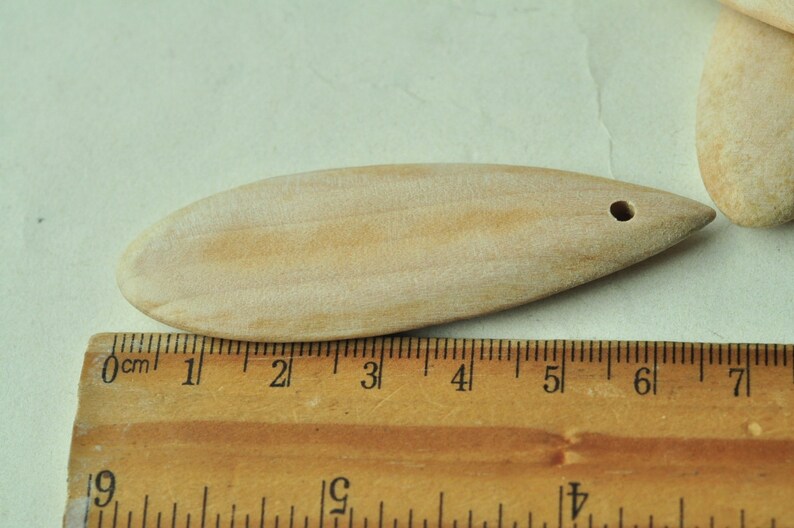 May include: A light brown wooden spoon with a hole at the top, measuring approximately 5 inches long. The spoon is resting on a wooden ruler.