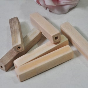 May include: A collection of unfinished wooden beads, rectangular in shape, with a hole drilled through the center of each. The beads vary in color from light beige to a darker brown, with visible wood grain. These beads are suitable for jewelry making and crafts.