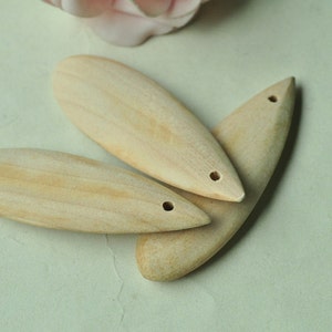 May include: Three wooden teardrop-shaped pendants with a hole at the top. The pendants are light brown and have a smooth, polished finish.