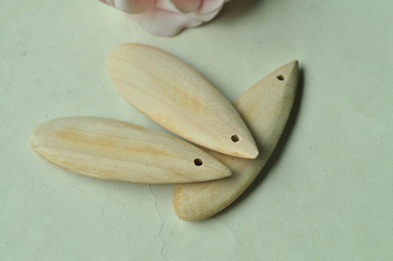 May include: Three wooden teardrop-shaped pendants with a hole at the top. The pendants are light brown and have a smooth, polished finish.