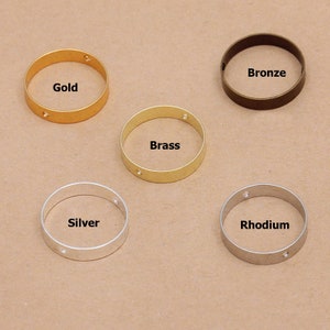May include: Five metal rings in different finishes: gold, brass, bronze, silver, and rhodium. Each ring has two small holes.
