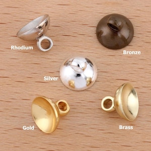 May include: A selection of metal jewellery findings in rhodium, bronze, silver, gold, and brass finishes. Each finding has a rounded cap shape with a loop for attachment. Text labels identify each finish in the image.