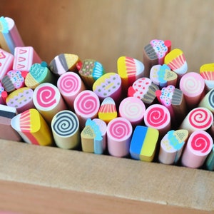 May include: A collection of colorful polymer clay canes, each intricately designed to resemble miniature desserts. The assortment includes cupcakes, ice cream cones, cakes, and spiral candies, all arranged in a wooden box. These are perfect for crafting.