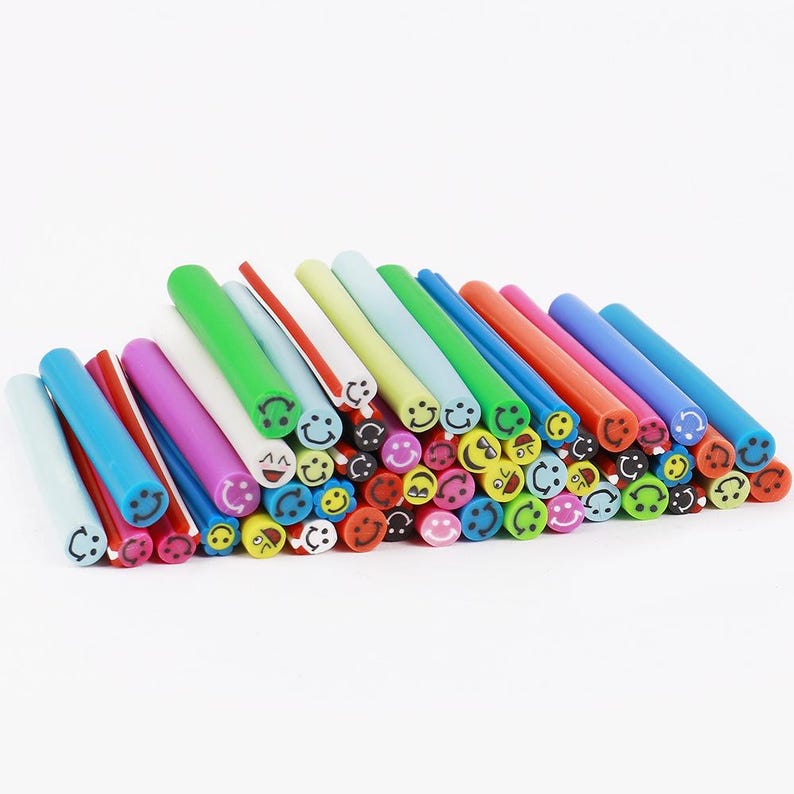 May include: A collection of colorful, cylindrical craft beads with smiley face designs. The beads are in various colors, including blue, green, red, and yellow. The ends of the beads feature different smiley face expressions.