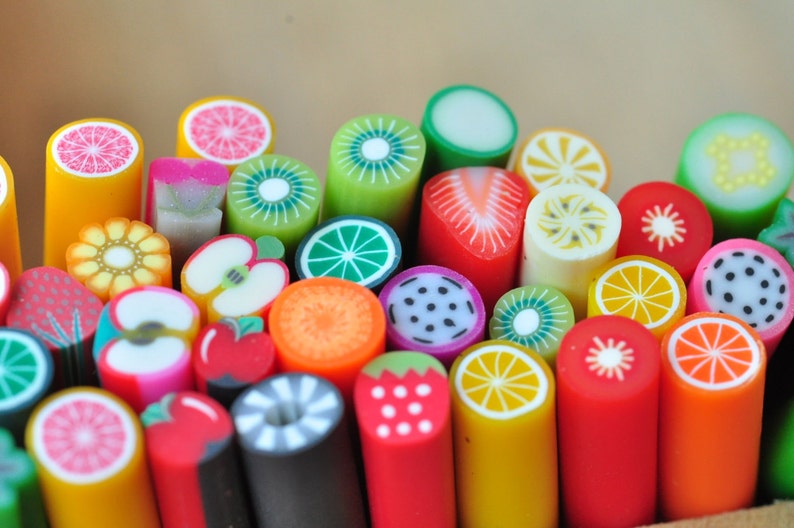 May include: A collection of colorful polymer clay fruit slices, including oranges, kiwis, strawberries, and lemons. The slices are cylindrical and feature detailed designs, perfect for crafting or jewelry making. The vibrant colors and variety of fruit designs are eye-catching.