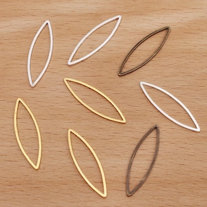 Puede incluir: Ocho hallazgos de joyería ovalados de metal en tres colores: plata, oro y bronce. Los hallazgos están dispuestos en un patrón aleatorio sobre una superficie de madera.