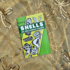 May include: A green and yellow pamphlet titled "HALL'S SHELLS OF THE FLORIDA COASTS" with a price tag of $1.95. The pamphlet features illustrations of various seashells.