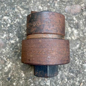 May include: A close-up of a rusty metal tool with the text "E-USA-500" and "1-1/4 CONDUIT" etched into the metal. The tool has a cylindrical shape with a hexagonal base.