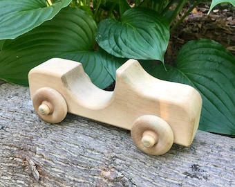 May include: A wooden toy car with a simple design, featuring a rounded body and two large wheels. The car is made of natural wood and has a light brown color.