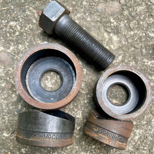 May include: A collection of metal tools, including a bolt and several conduit punches. The punches are labeled with size specifications. The tools have a weathered, used appearance, suggesting they are for industrial or construction use.