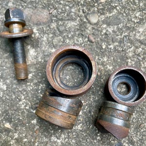 May include: A collection of rusty metal tools, including a bolt with a hexagonal head and several cylindrical pieces. The pieces have a dark, aged appearance, suggesting they are well-used. Some pieces have text that is difficult to read.