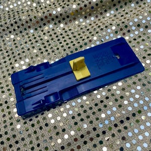 May include: A blue plastic toy car carrier with a yellow ramp. The carrier has slots for holding toy cars and a hinged ramp for loading and unloading. The carrier is made of durable plastic.
