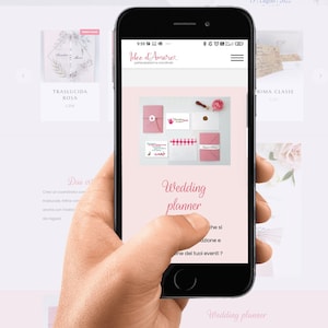 May include: A screenshot of a mobile phone displaying a website for wedding planning services. The website features a pink and white color scheme and the text "Wedding planner" is prominently displayed. The website also includes a photo of a wedding invitation suite with a pink envelope, a white card, and a wax seal.