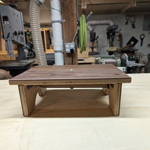 May include: A small wooden step stool with a brown top and light brown sides. The stool is made of plywood and has a simple design.