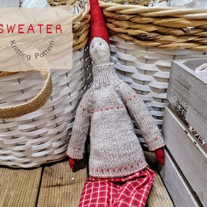 Könnte beinhalten: Ein Strickmuster für einen Gnom-Pullover. Der Pullover ist hellbeige mit roten Akzenten. Der Gnom trägt den Pullover und eine rot-schwarze karierte Hose. Die Puppe sitzt in einem weißen Weidenkorb.