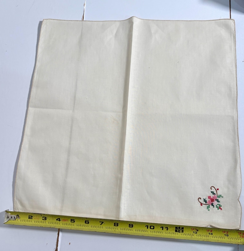 May include: Off-white linen handkerchief with a small embroidered floral design in the corner. The design includes red, pink, and green elements. The handkerchief measures approximately 14 inches long.