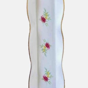 May include: A white, rectangular ceramic serving dish with a wavy edge and gold trim. The dish is decorated with clusters of pink roses and green leaves. A decorative piece for serving appetizers or desserts.