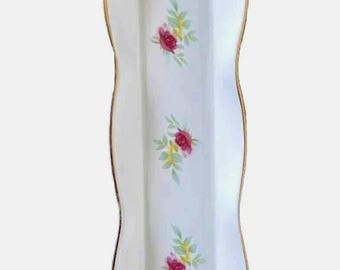 May include: A white, rectangular ceramic serving dish with a wavy edge and gold trim. The dish is decorated with clusters of pink roses and green leaves. A decorative piece for serving appetizers or desserts.