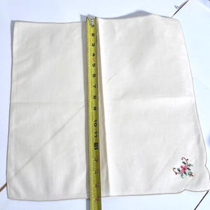 May include: Cream-colored handkerchief with a floral embroidery in the corner. The handkerchief measures approximately 12 inches in length. The embroidery features pink and green flowers with red accents.