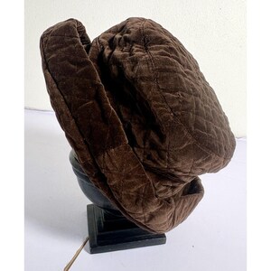 May include: A dark brown quilted hat with a soft, textured fabric surface. The hat features a distinct diamond-shaped stitching pattern across the entire exterior, including the wide, folded brim that encircles the crown of the headpiece.
