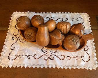 Puede incluir: Un cuenco de madera lleno de fruta de madera tallada. El cuenco es marrón y tiene forma de hoja. La fruta es de diversas formas y tamaños, incluyendo manzanas, peras y una carambola. El cuenco está sobre un mantel de encaje blanco.