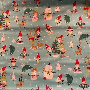 May include: Light blue fabric featuring a repeating Christmas pattern of gnomes in red hats, snowmen, reindeer, squirrels, and decorated pine trees. The selvage edge includes the text Michael Miller Fabrics LLC, All Rights Reserved.