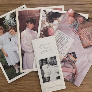 Puede incluir: Una colección de publicaciones vintage de costura y bordado, incluyendo un "Heirloom Sewing Catalog" y un libro titulado "Antique Embroidery". Las imágenes presentan mujeres con vestidos blancos y diseños de bordado detallados. Los artículos están dispuestos sobre una superficie de madera.