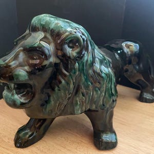 May include: A ceramic lion figurine with a glossy finish. The lion's mane is a mix of green and brown, while the body is black. The lion is in a roaring pose, with its mouth open. The figurine is a decorative item.