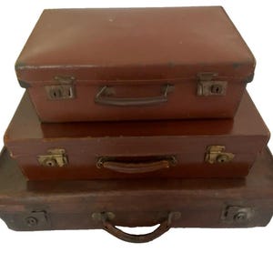 May include: A stack of three rectangular brown suitcases of varying sizes. Each suitcase features a top handle, metal latches, and a structured design. The suitcases are arranged with the smallest on top and the largest on the bottom.