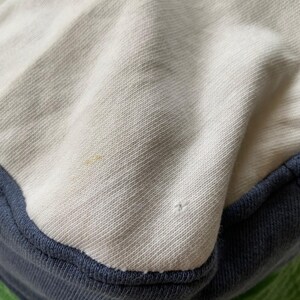 May include: Close-up of a white and blue bucket hat. The hat has a white crown, a navy blue brim, and a green underside. The fabric appears to be a soft, textured material.