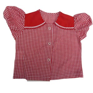 May include: A red and white gingham blouse with a red collar and puffed sleeves. The collar is trimmed with white lace, and the blouse fastens with three white buttons. A classic, vintage-style top.
