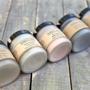 May include: Five glass jars with black lids containing different types of clay masks. The labels on the jars read "Moonrise Creek", "Alchemy of the Sea Seaweed Clay Mask", "Green Divinity Clay Mask", "Rose & Clay Pink Clay Mask", and "Charcoal Detox Clay Mask".