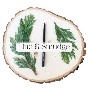 May include: A black cosmetic pencil with the text Moonrise Cheek printed on the side, positioned vertically between two green cedar sprigs on a round, light-colored wooden slice. A white rectangular overlay displays the text Line & Smudge.