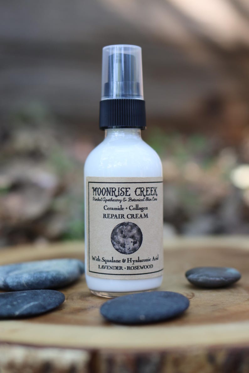 Peut inclure: Une bouteille blanche de cr&egrave;me r&eacute;paratrice Moonrise Creek avec une pompe et un bouchon noirs. L'&eacute;tiquette indique "Cr&egrave;me r&eacute;paratrice C&eacute;ramide + Collag&egrave;ne" et &eacute;num&egrave;re les ingr&eacute;dients. La bouteille est entour&eacute;e de pierres grises lisses.
