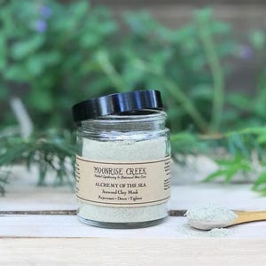 May include: A glass jar of green seaweed clay mask with a black lid. The label reads "Moonrise Creek Herbal Apothecary & Botanical Skin Care Alchemy of the Sea Seaweed Clay Mask Rejuvenate - Detox - Tighten"