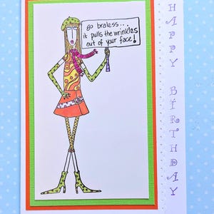 May include: A whimsical birthday card with a cartoon illustration of a woman holding a sign that reads "Go braless... it pulls the wrinkles out of your face!". The card has a white background with orange and green borders, and the words "Happy Birthday" are written vertically.