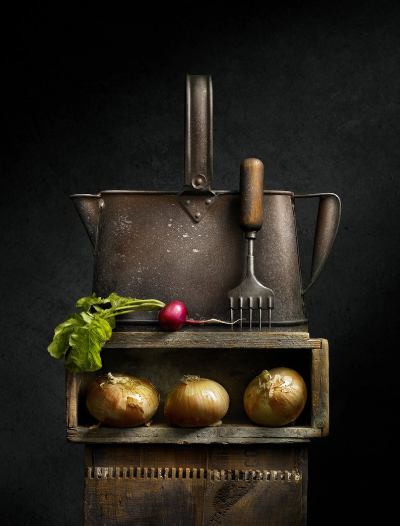 May include: A still life composition featuring a rustic metal pitcher, a vintage kitchen tool, and a wooden crate holding three onions. A radish with green leaves rests on the crate. The scene is set against a dark background.
