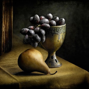 May include: A still life composition featuring a pear and a bunch of dark grapes spilling from a decorative, aged ceramic chalice. The chalice has a textured, dripped glaze. The fruit rests on a golden-brown cloth, with a dark background.