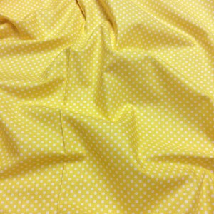 May include: Yellow fabric with white polka dots. The fabric is creased and has a soft texture.