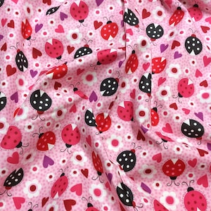 May include: Pink fabric with a repeating pattern of red and black ladybirds, hearts, and white flowers.