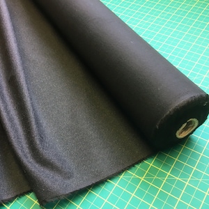 May include: A roll of black fabric with a slightly textured surface. The fabric is rolled up and secured with a brown cardboard tube.
