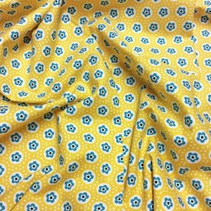 May include: Yellow fabric with a repeating pattern of blue and white flowers. The fabric is folded and creased.