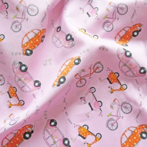 May include: Pink fabric with a repeating pattern of cars, bicycles, and scooters. The cars are orange with white polka dots, the bicycles are red with white accents, and the scooters are pink with white accents. The fabric has the text "now we're join places!" repeated throughout.