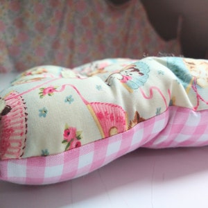 May include: A pink and white gingham cushion with a cream fabric top featuring a repeating pattern of kittens and flowers.