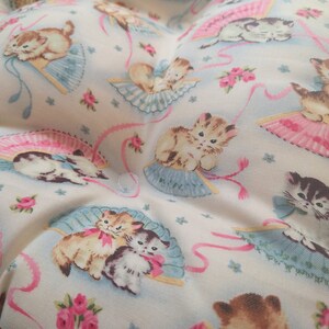 May include: White fabric with a repeating pattern of kittens holding pink and blue fans. The kittens are brown, black, and white.