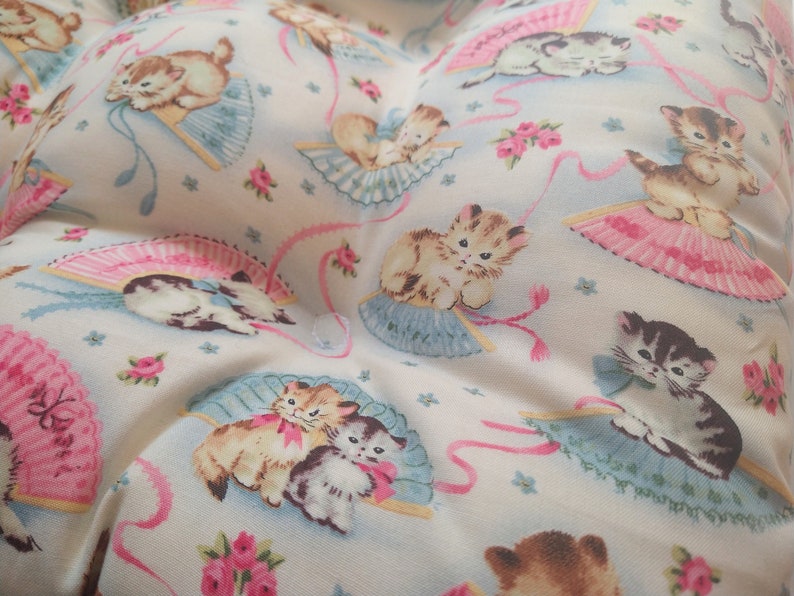 May include: White fabric with a repeating pattern of kittens holding pink and blue fans. The kittens are brown, black, and white.
