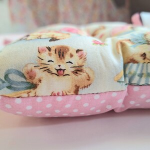 May include: A pink and white polka dot cushion with a light blue background featuring a repeating pattern of kittens and flowers.