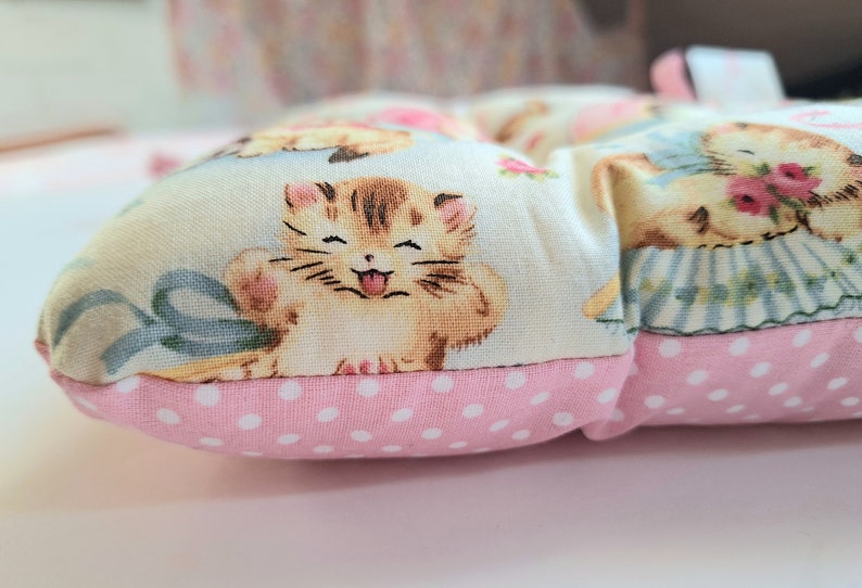 May include: A pink and white polka dot cushion with a light blue background featuring a repeating pattern of kittens and flowers.